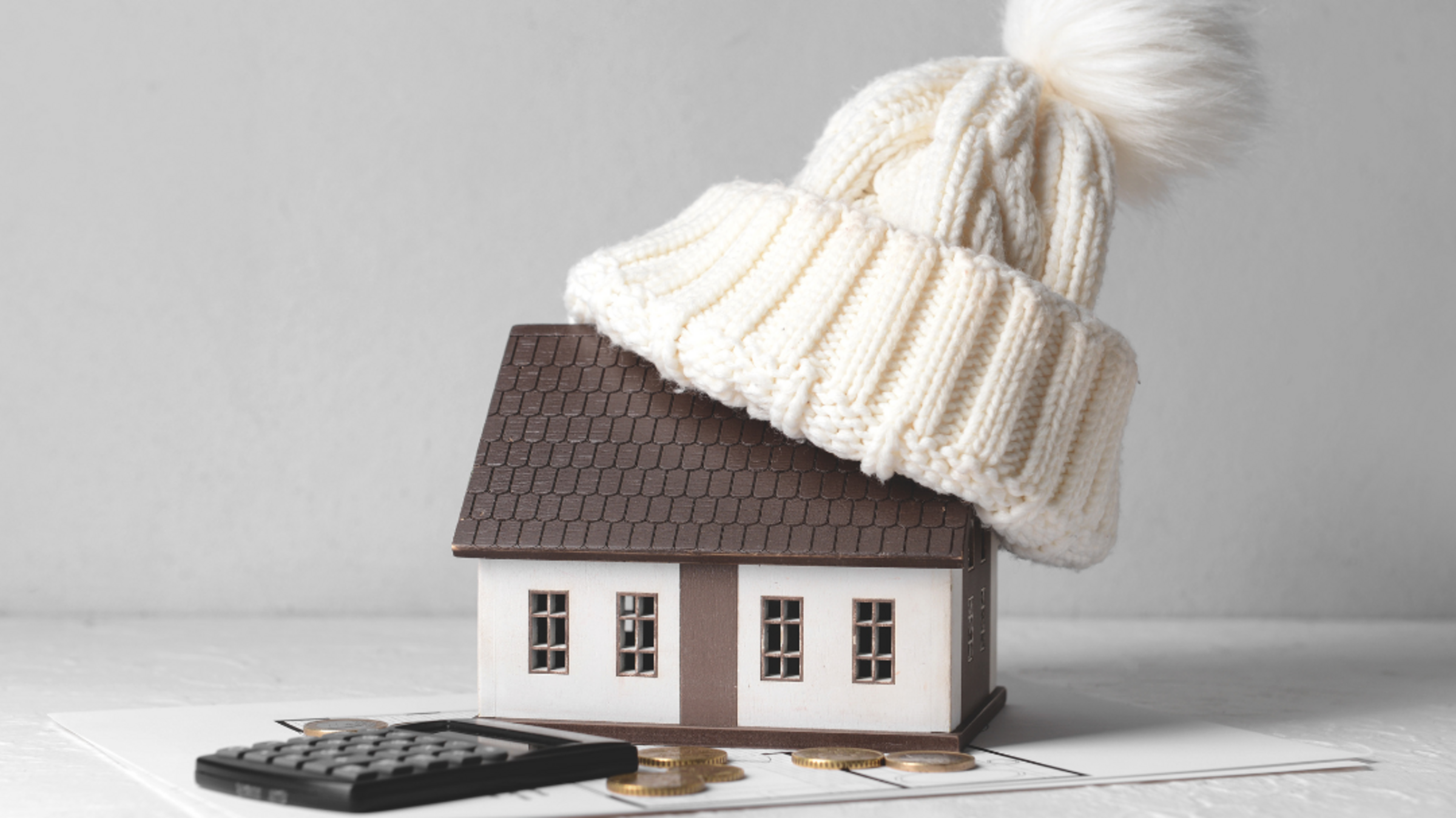 Spielzeughaus mit Wollmütze auf dem Dach.  Abgebildet ist noch ein Taschenrechner und Kleingeld